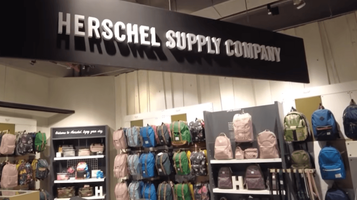 The interior of a Herschel Supply Company store featuring a large black logo sign above a display of colorful backpacks.