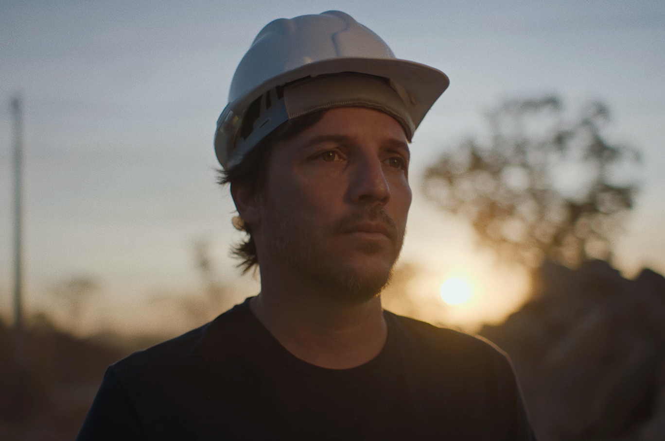 Um homem com capacete de segurança branco com um pôr do sol ao fundo.
