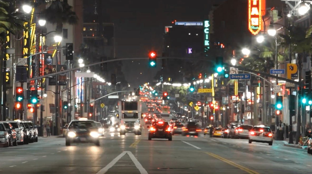 A busy street at night in Los Angeles with heavy traffic, glowing streetlights, and colorful neon signs