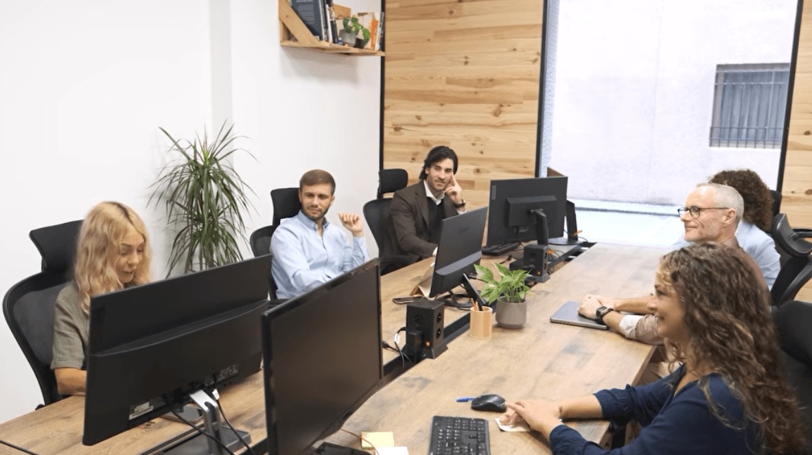 A group of colleagues working at a large wooden conference table in an office.