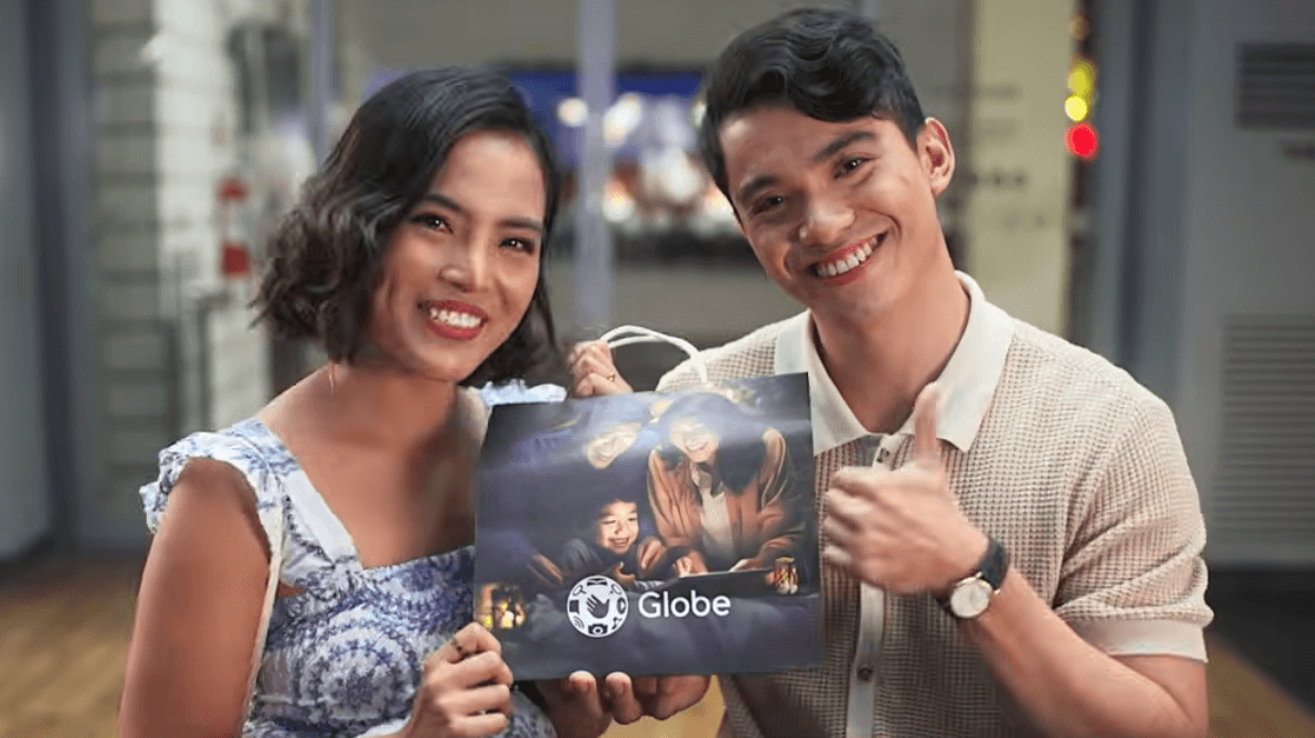 A smiling woman and a man giving a thumbs up hold a shopping bag featuring the Globe Telecom logo